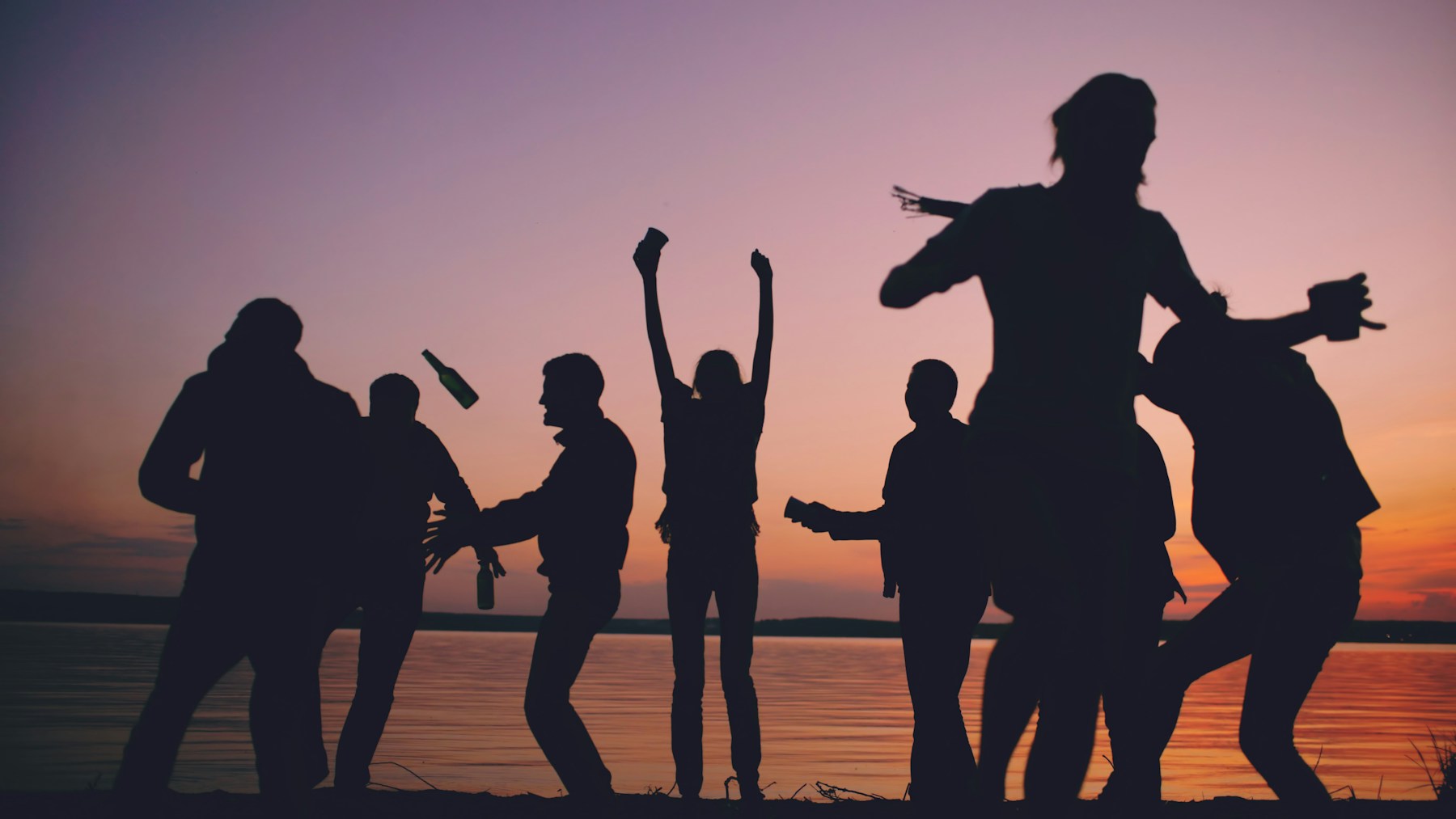 Friends dancing together beside the sea at sunset